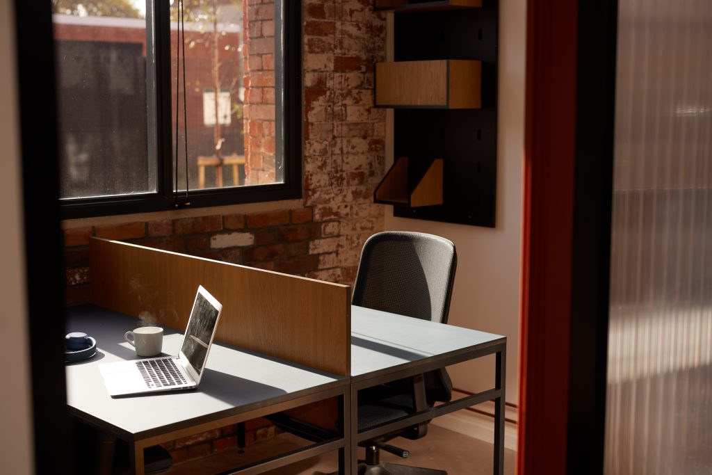A laptop on a desk next to a steaming cup of coffee.