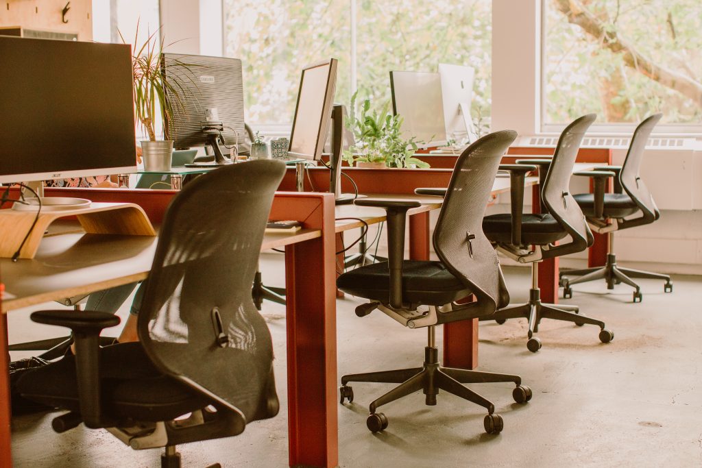 Red metal desks with wheeled office chairs in an office space.
