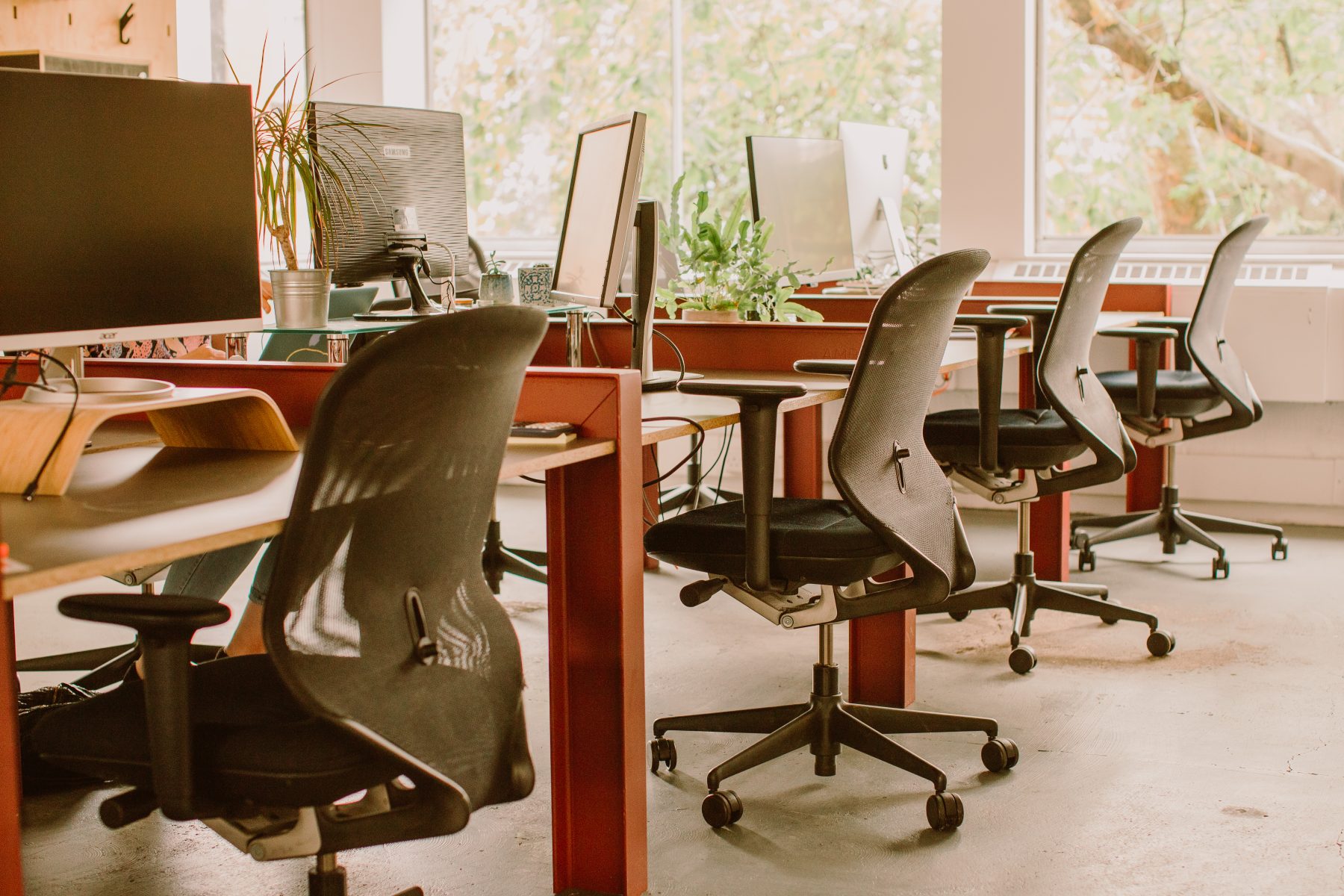 Red metal desks with wheeled office chairs in an office space.