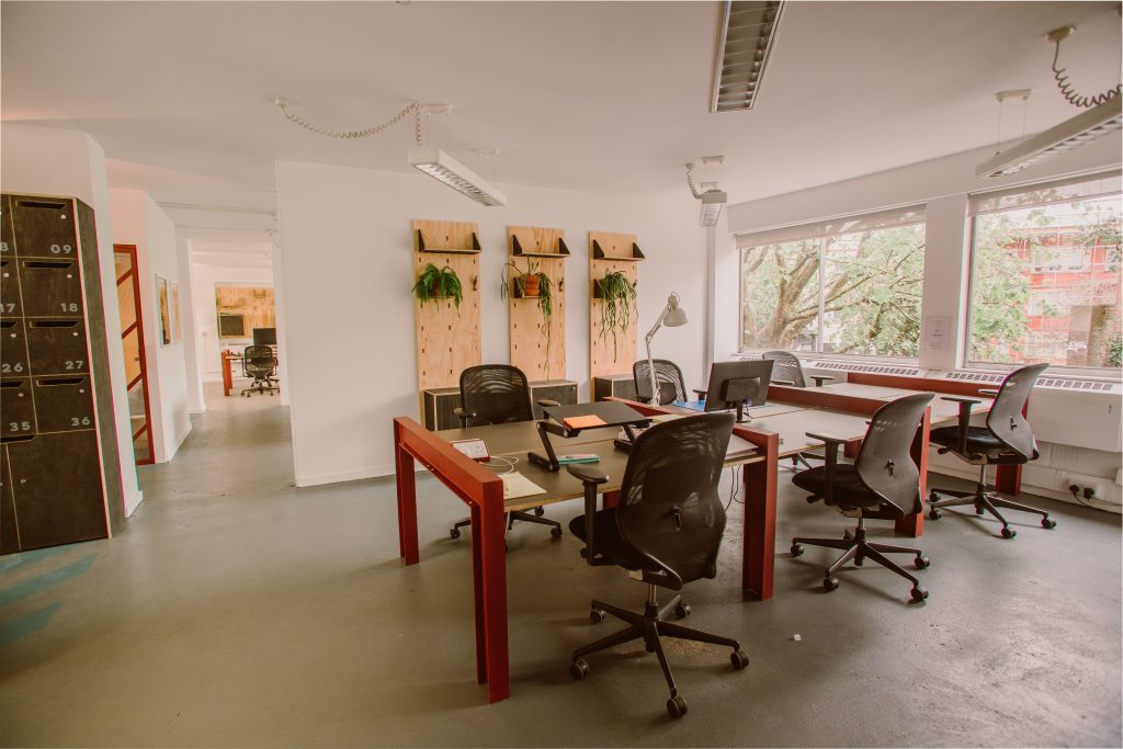 A modern coworking space with desks spaces, plants and concrete floor.