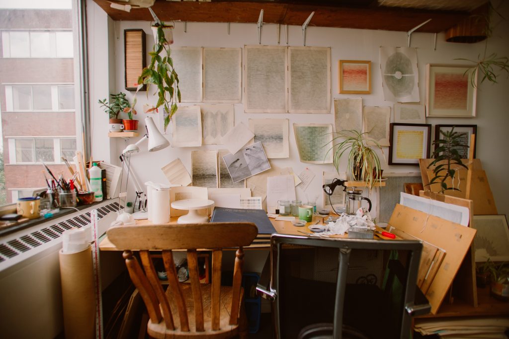 Artist workspace with wooden chair, and paperwork art on the walls