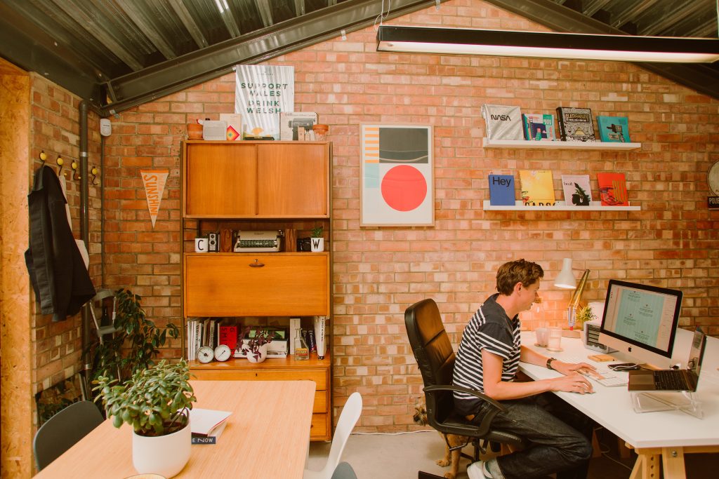 Man sat at a desk working on a macbook computer in an office with plants and cabinets