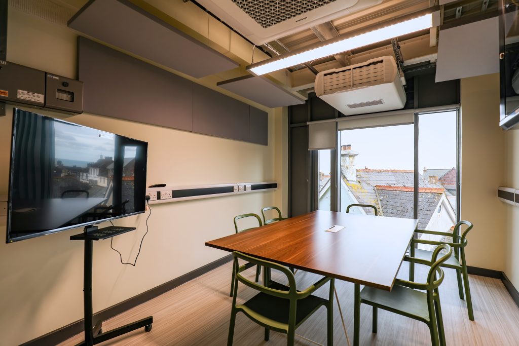 A meeting room with a table and chairs, TV screen and a view over rooftops in the background