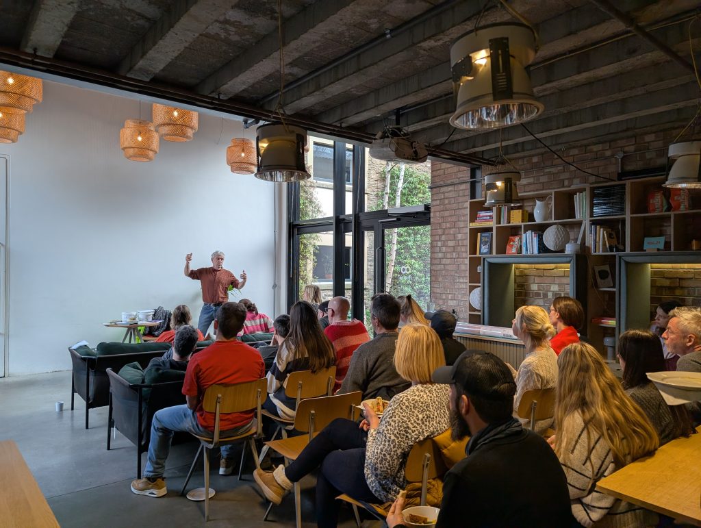 A man giving a presentation to a group of people sat in wooden chairs